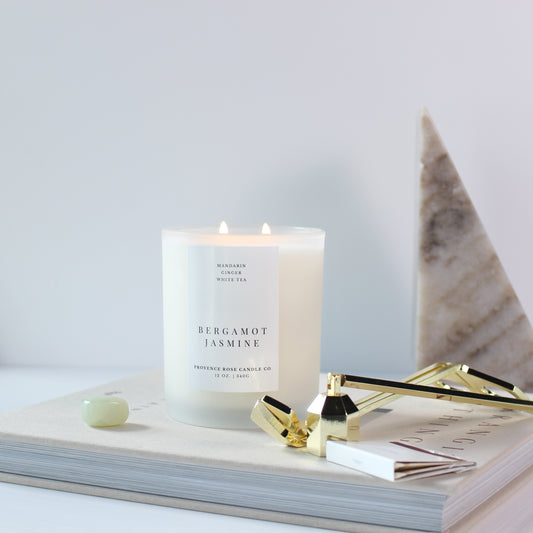 Candle labeled 'Bergamot Jasmine' on a book with a marble surface and gold accents.